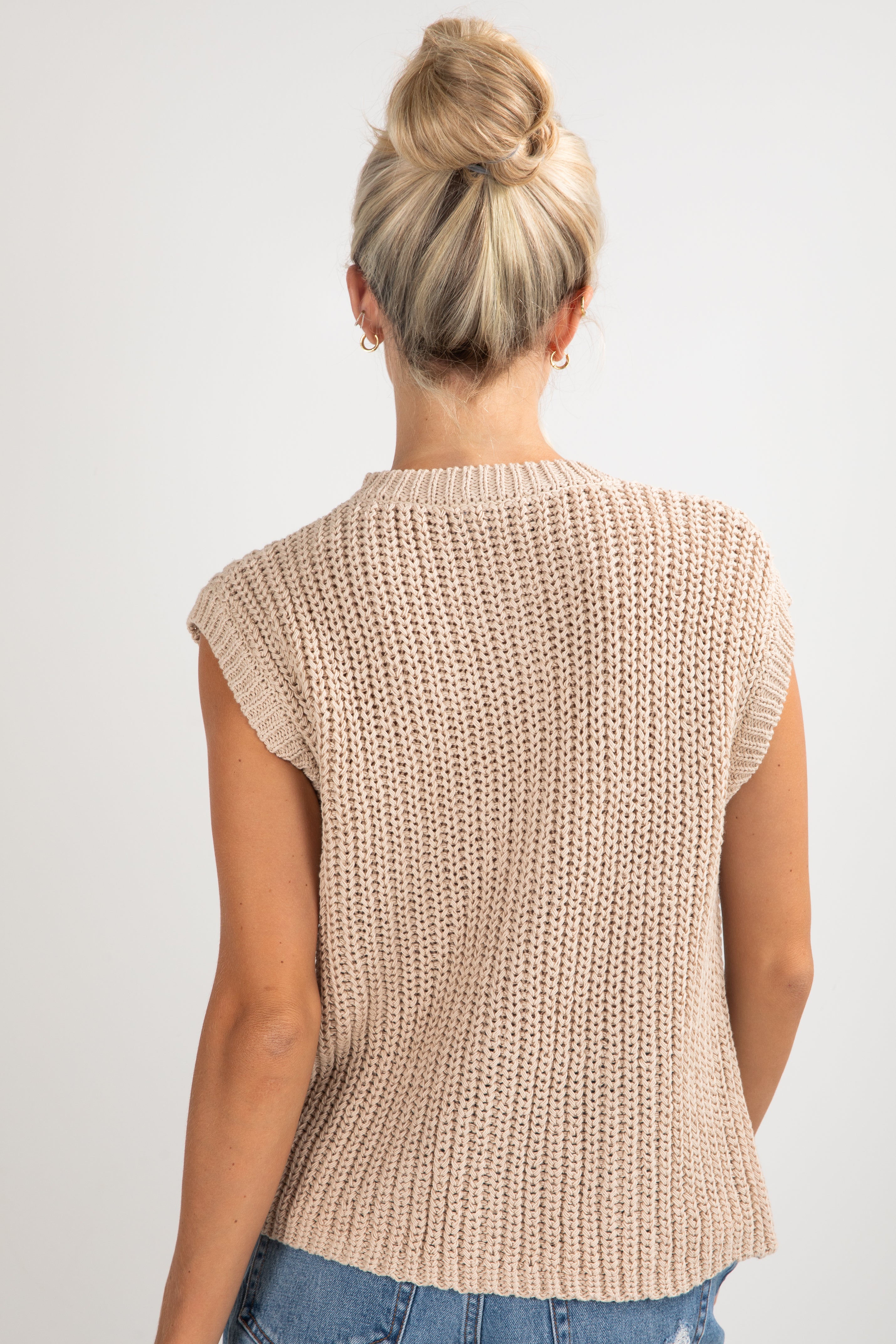 Person wearing a beige knitted vest on a plain background
