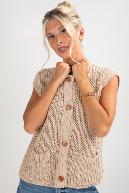 Woman wearing a beige knitted vest with buttons on a white background
