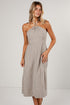 A woman modeling a halter-neck midi dress with vertical beige and white stripes, featuring a knotted neckline and side pockets, set against a plain light gray studio background.