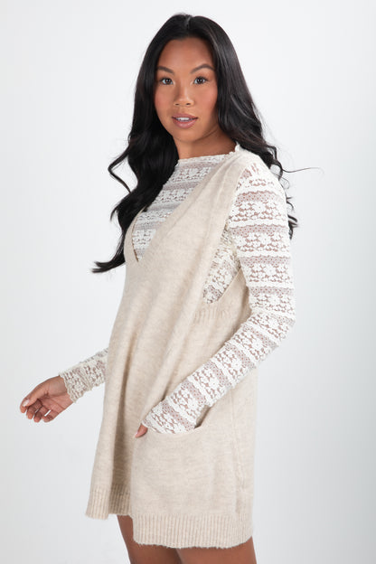 Woman wearing a beige sweater dress with lace sleeves on a white background