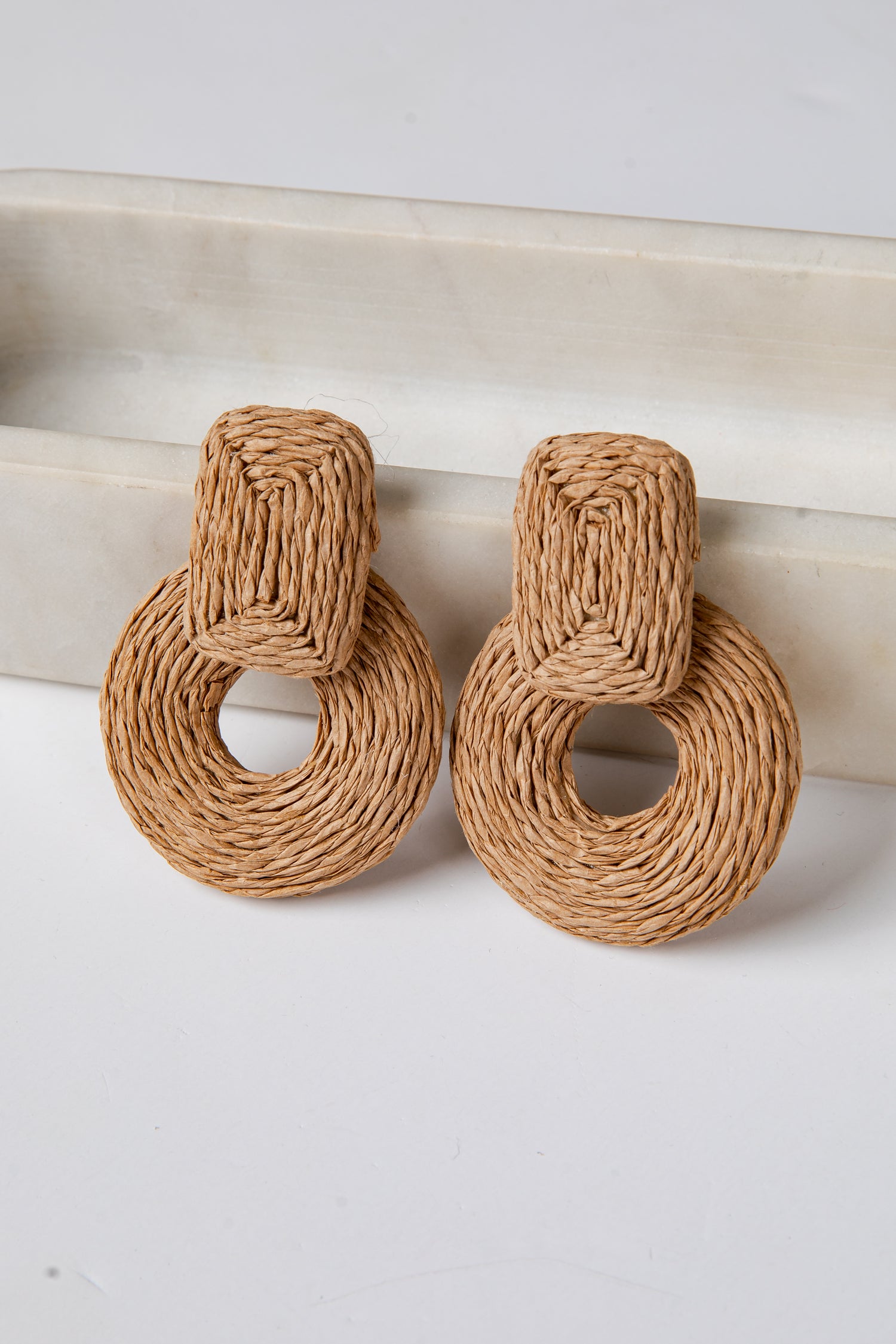 Pair of woven brown earrings on a white surface with a neutral background