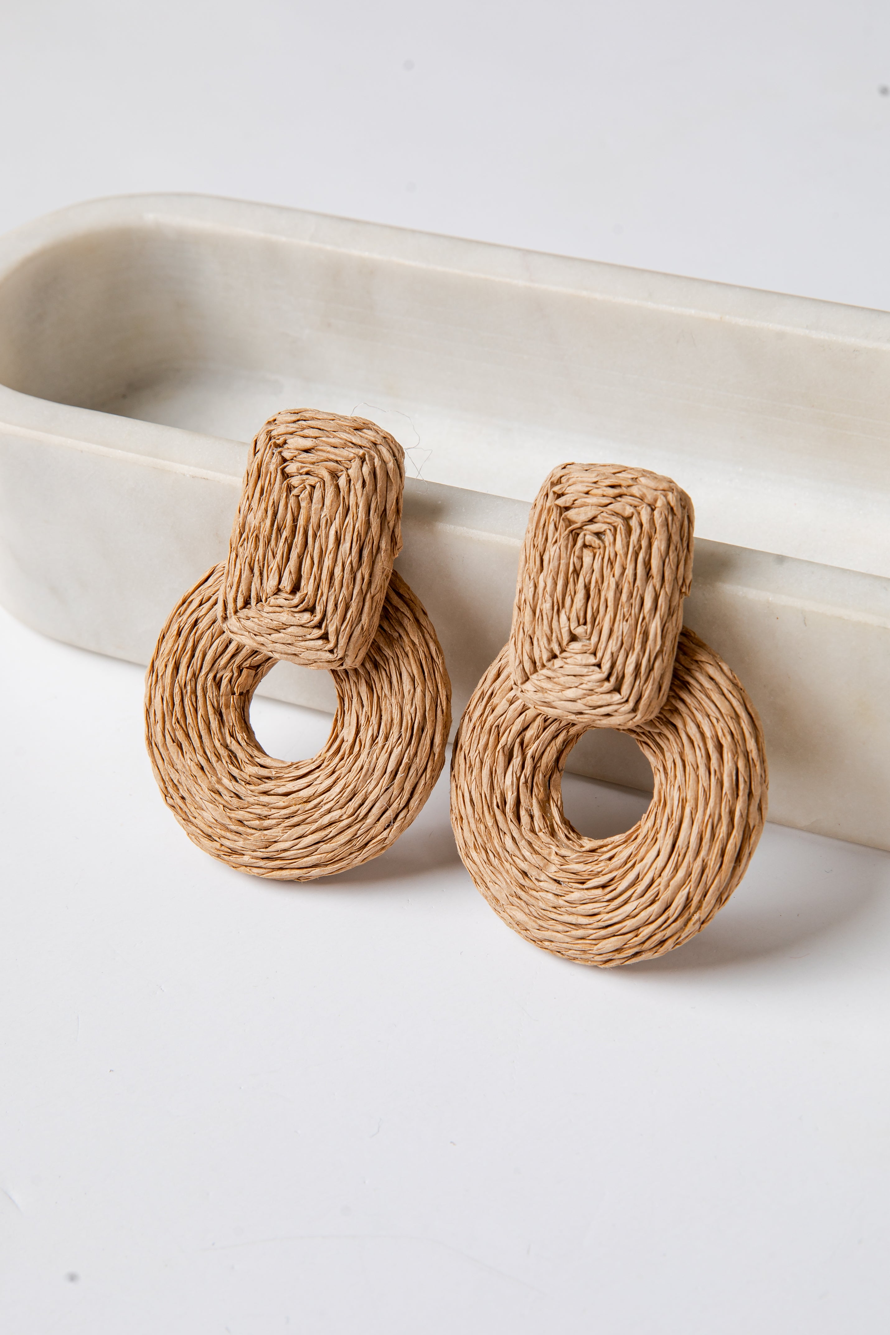 Pair of woven earrings on a white surface with a neutral background