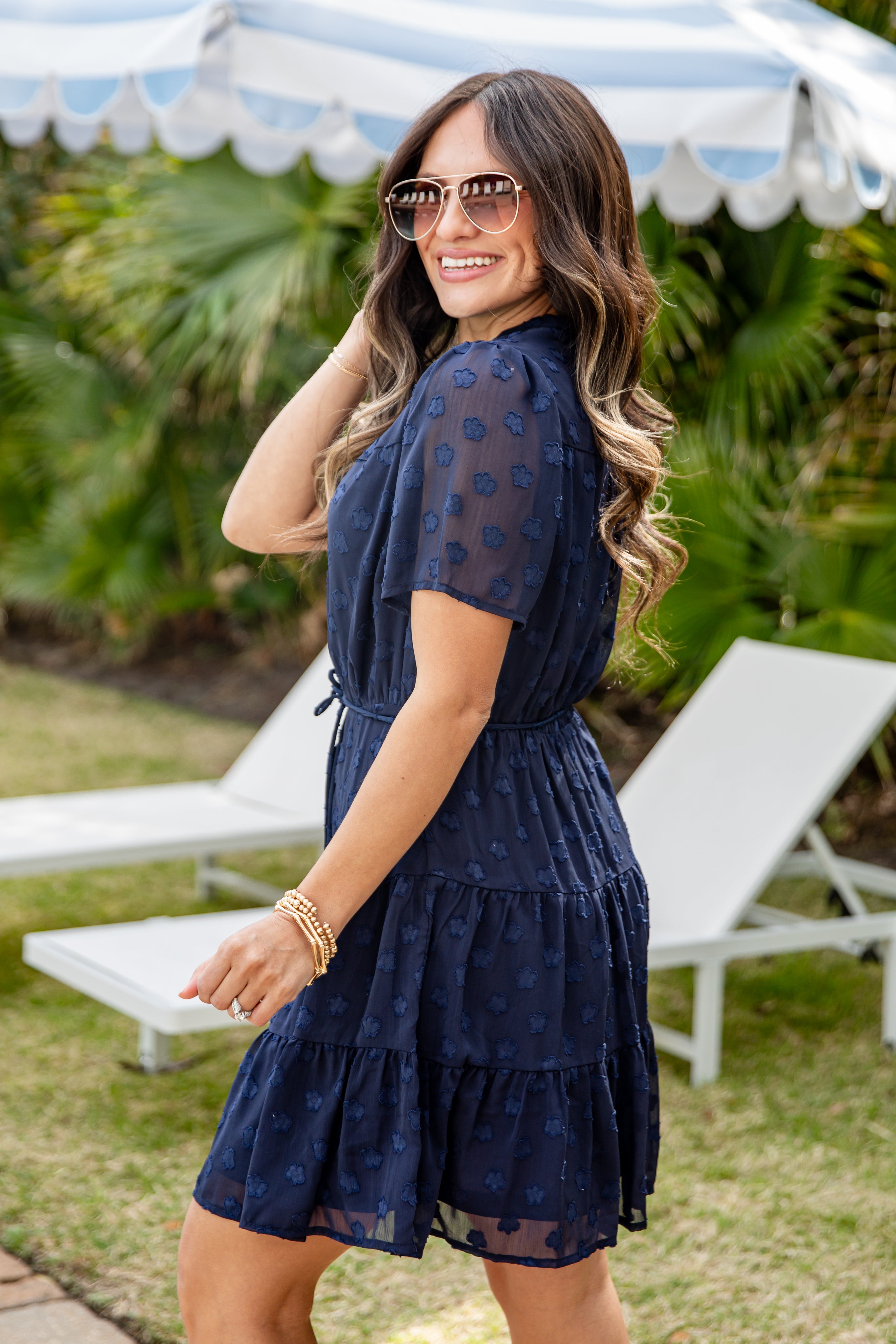 Woman in a navy blue dress standing outdoors with lounge chairs and greenery in the background