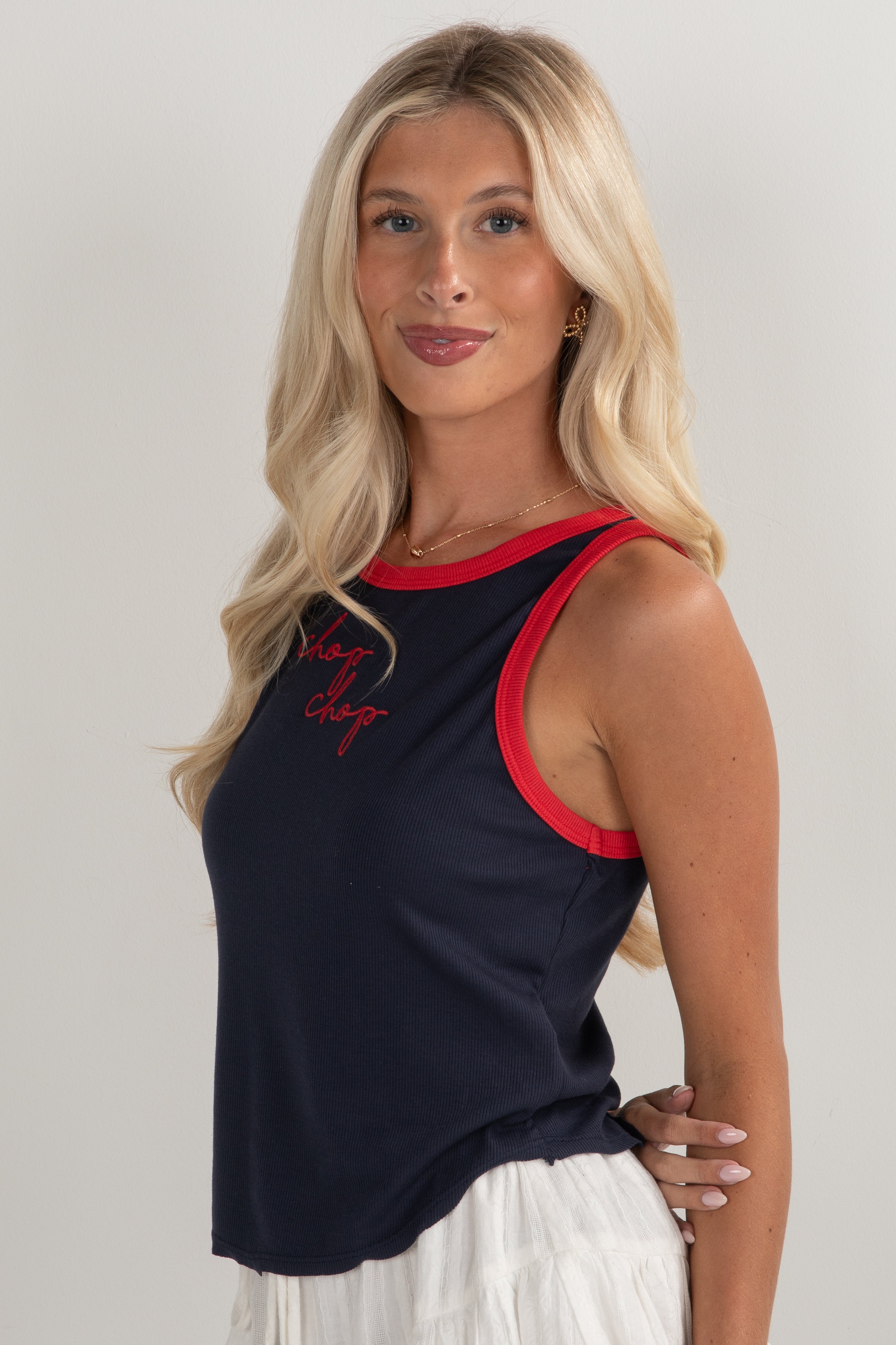 Woman wearing a navy tank top with red trim and white pants on a plain background