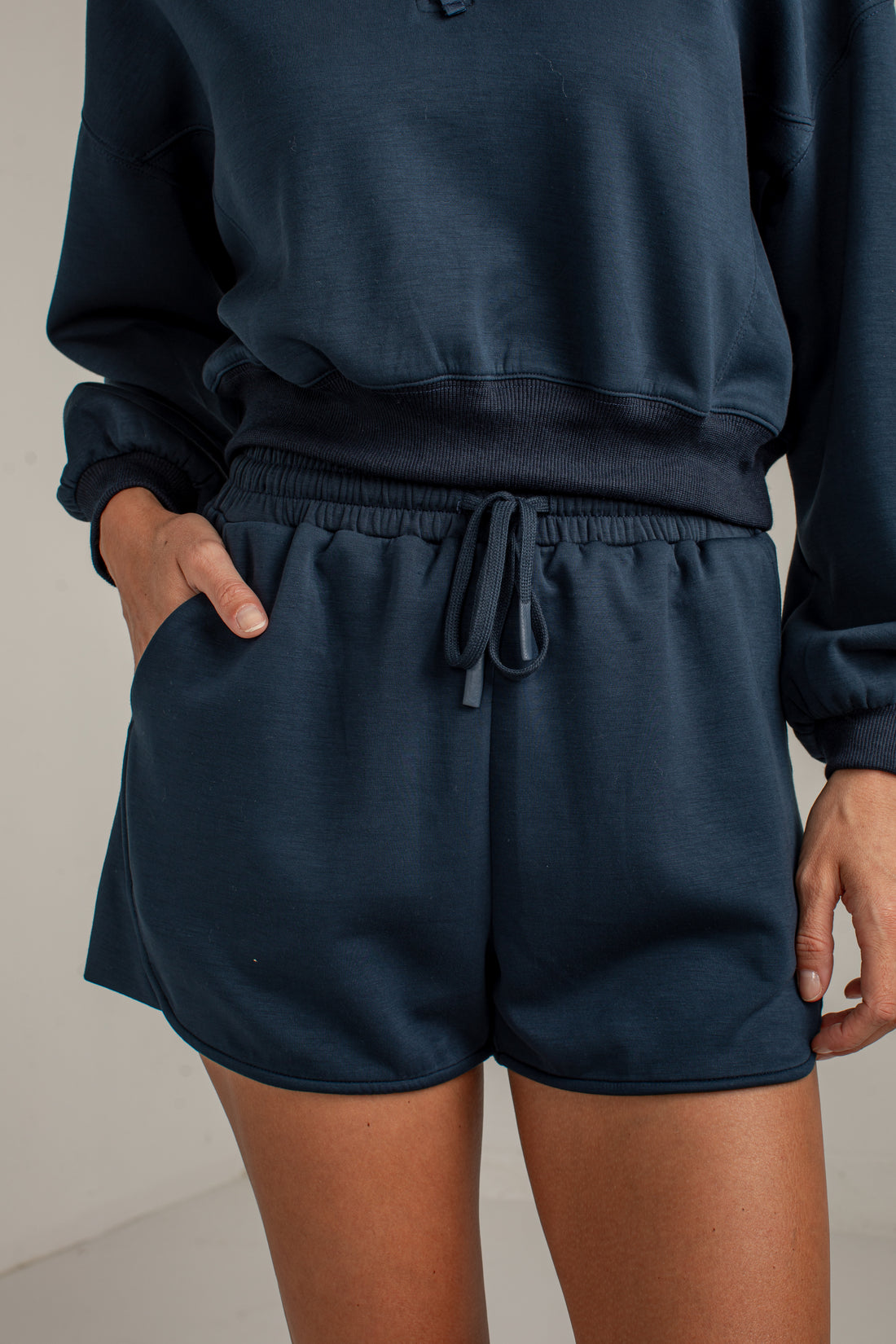 A person wearing dark navy blue lounge shorts with a drawstring waist and a matching navy sweatshirt, shown from the chest down against a plain light background.