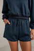 A person wearing dark navy blue lounge shorts with a drawstring waist and a matching navy sweatshirt, shown from the chest down against a plain light background.