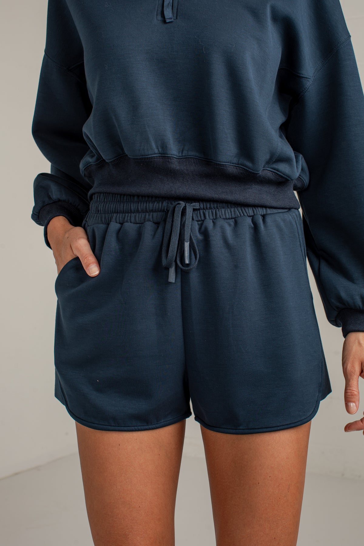 A person wearing a dark navy blue sweatshirt and matching drawstring shorts, shown from the chest down against a plain light background.