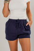 A person wearing navy blue drawstring shorts and a white top, shown from the chest to the upper thighs against a light gray studio background.