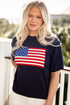 Woman wearing a navy sweater with an American flag design outdoors.