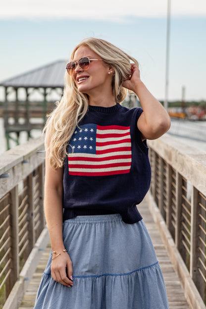 Woman wearing a navy sweater with an American flag design on a wooden pier.