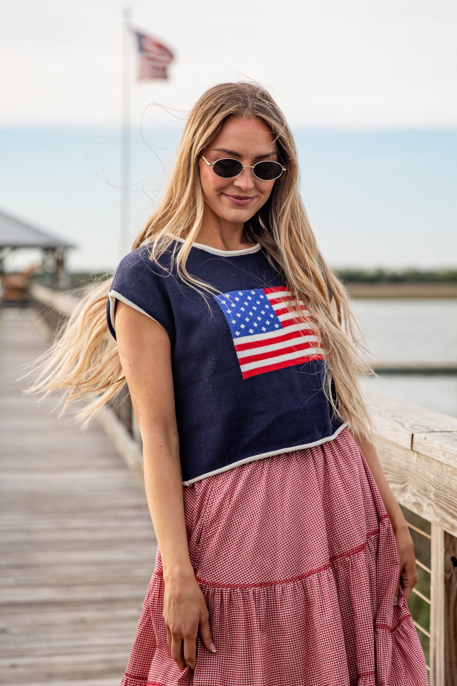 Woman wearing a navy blue t-shirt with an American flag design and a pink skirt on a dock.
