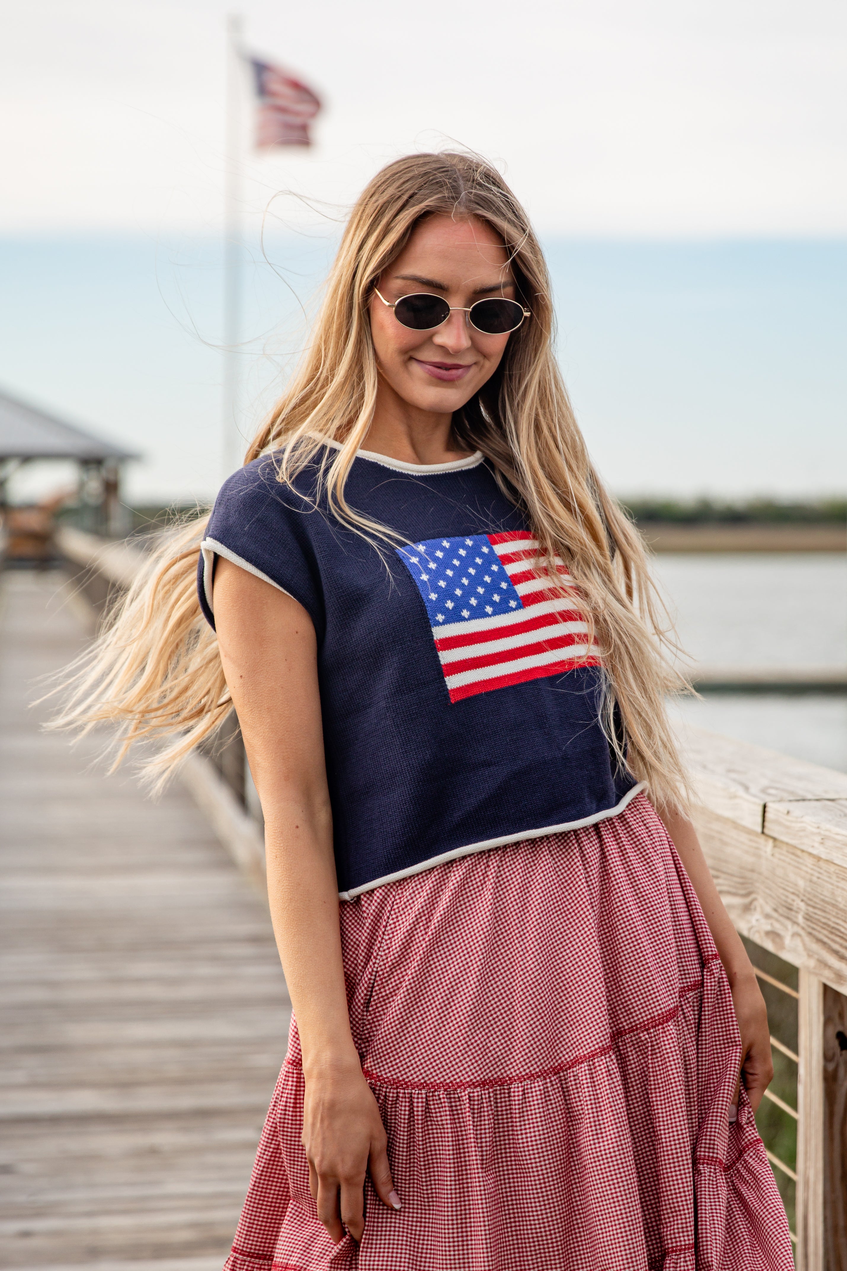 Woman wearing a navy blue t-shirt with an American flag design and a pink skirt on a dock.