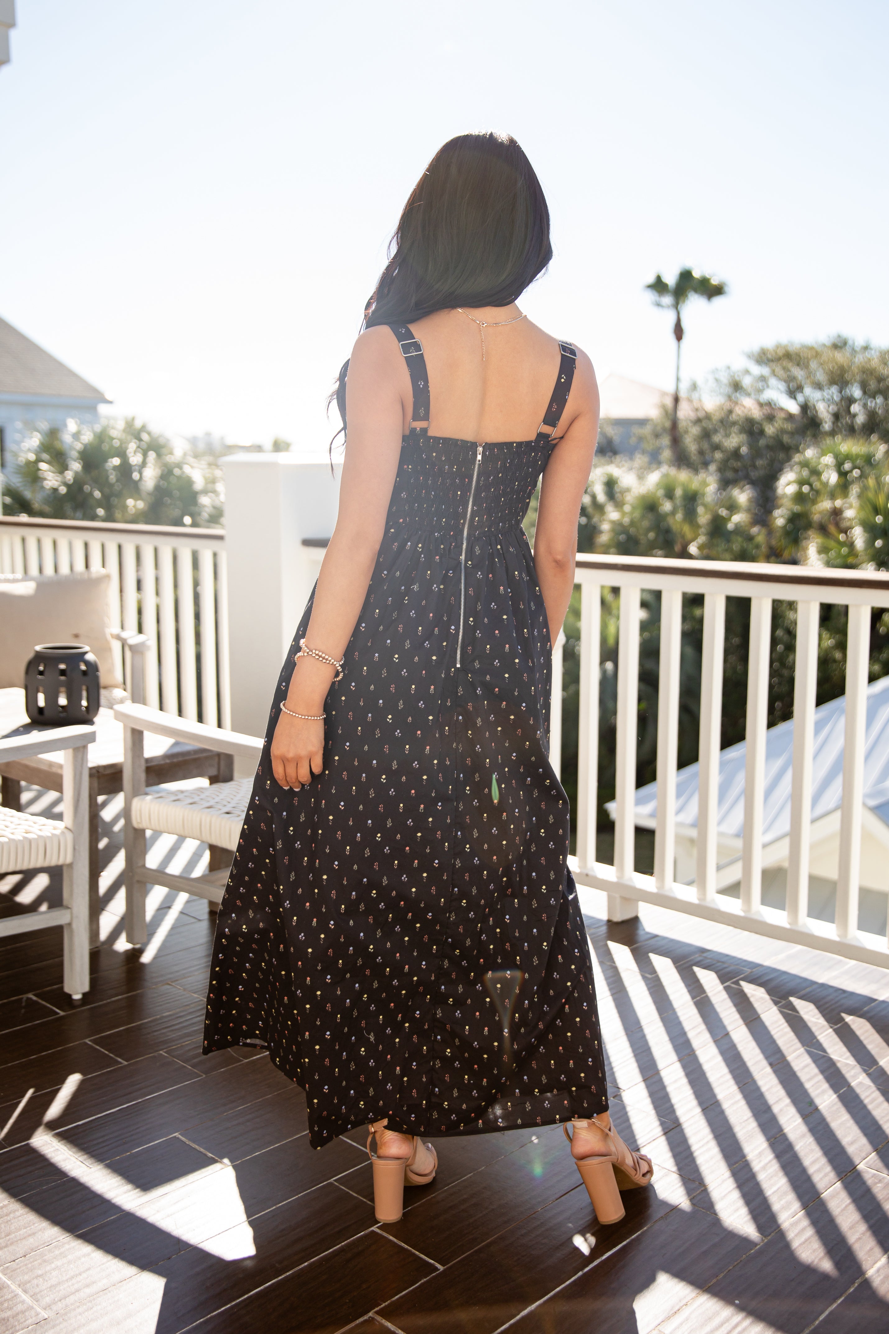 Woman in a black polka dot dress standing on a balcony with trees in the background