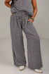 A person wearing loose black-and-white gingham wide-leg pants with a smocked waistband, paired with a matching top and white pointed shoes, photographed against a plain light gray studio background.