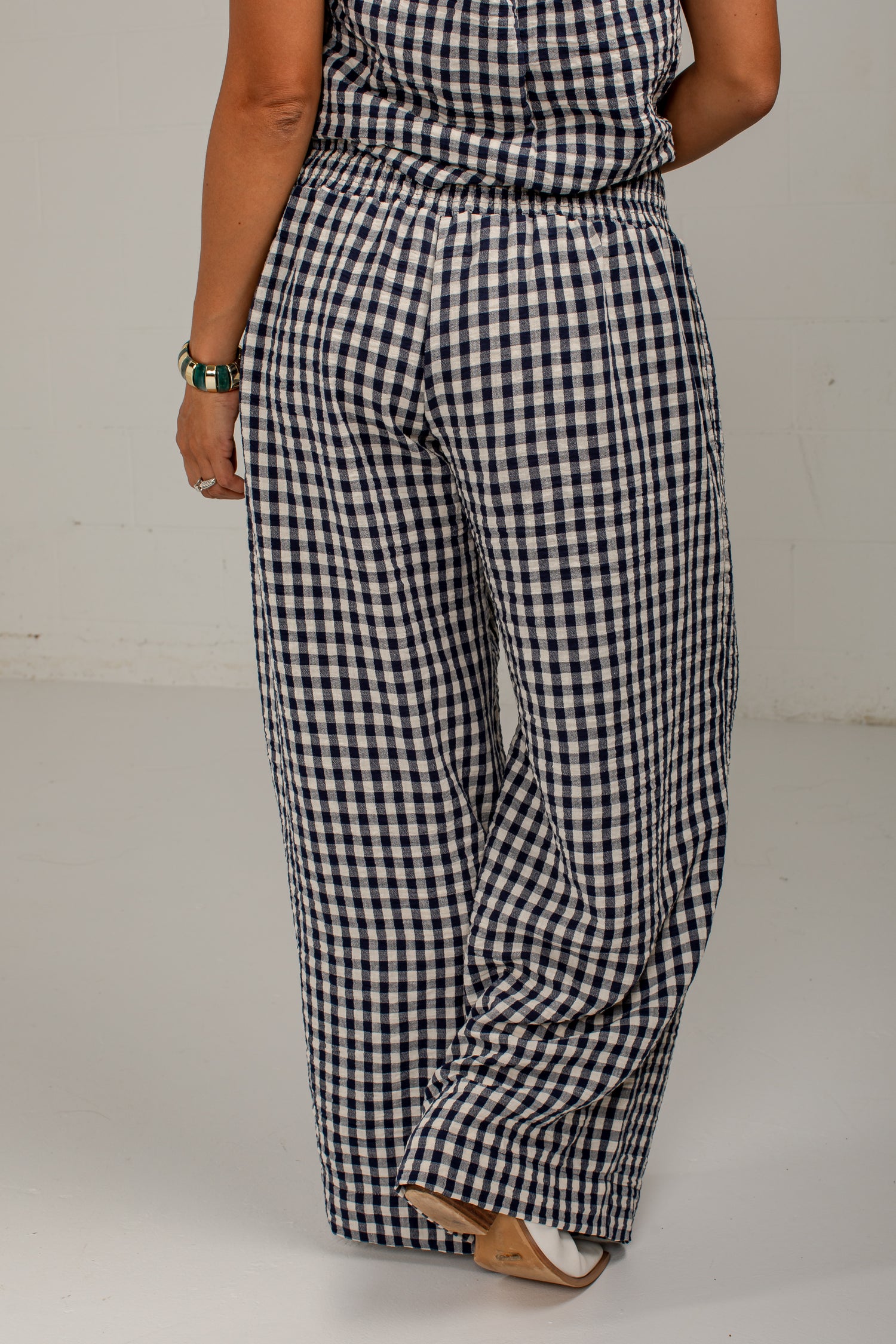 A person wearing loose, wide-leg pants with a navy and white gingham check pattern, shown from the back against a plain light gray studio background.
