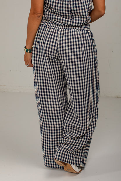A person wearing loose, wide-leg pants with a navy and white gingham check pattern, shown from the back against a plain light gray studio background.