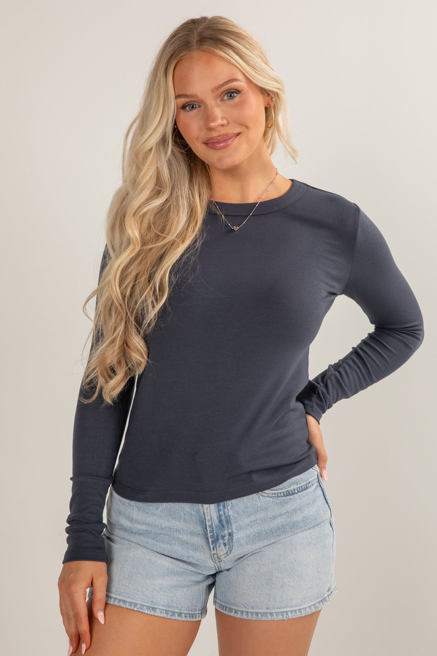 Woman wearing a dark blue long-sleeve top and denim shorts on a plain background