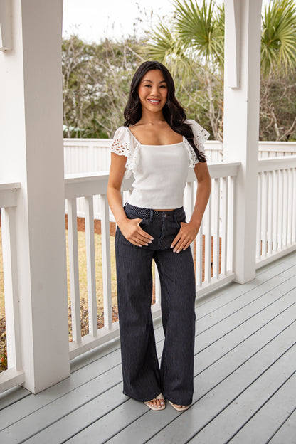 Woman standing on a porch wearing a white top and dark jeans.