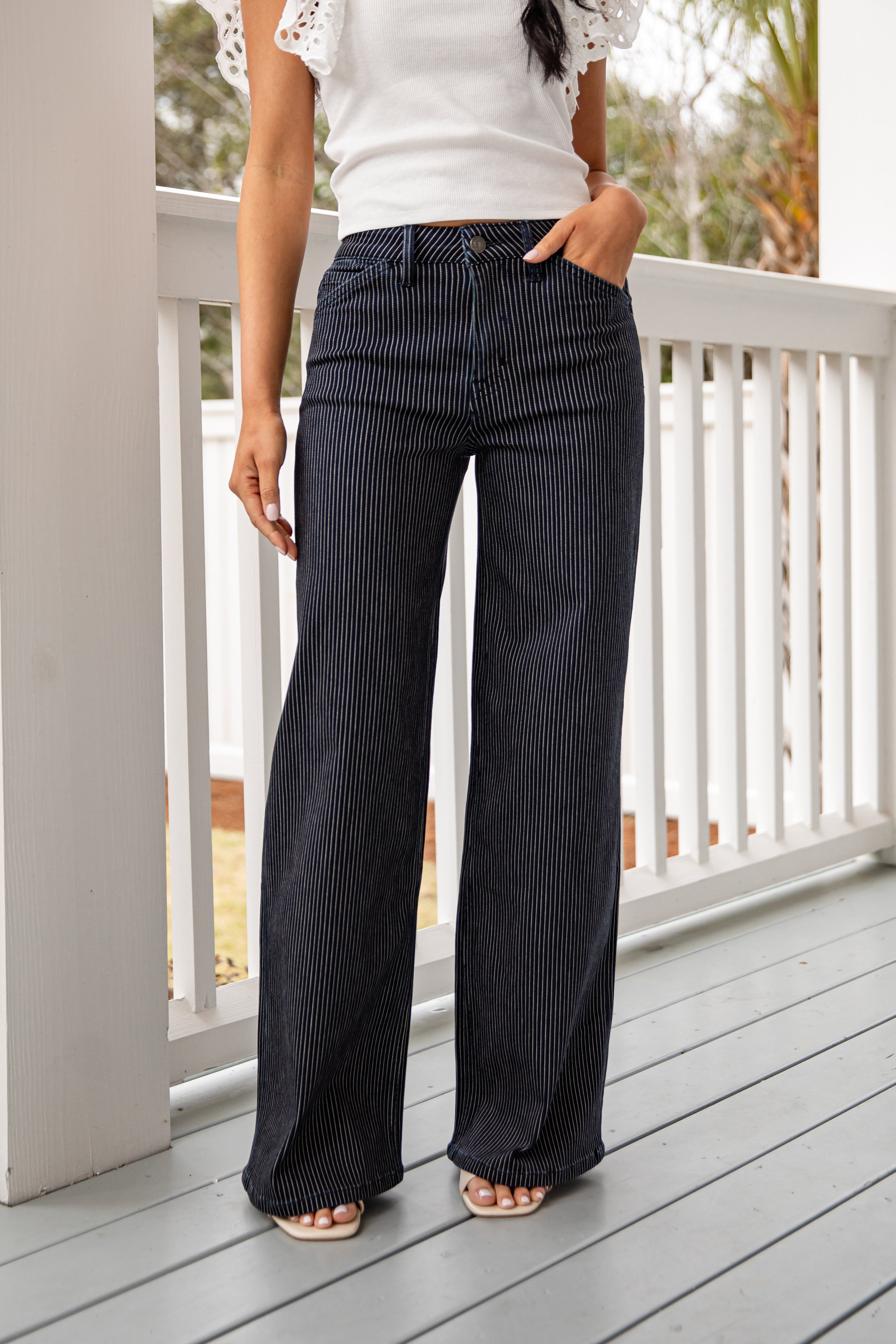 Person wearing black pinstripe pants and a white top on a wooden deck.