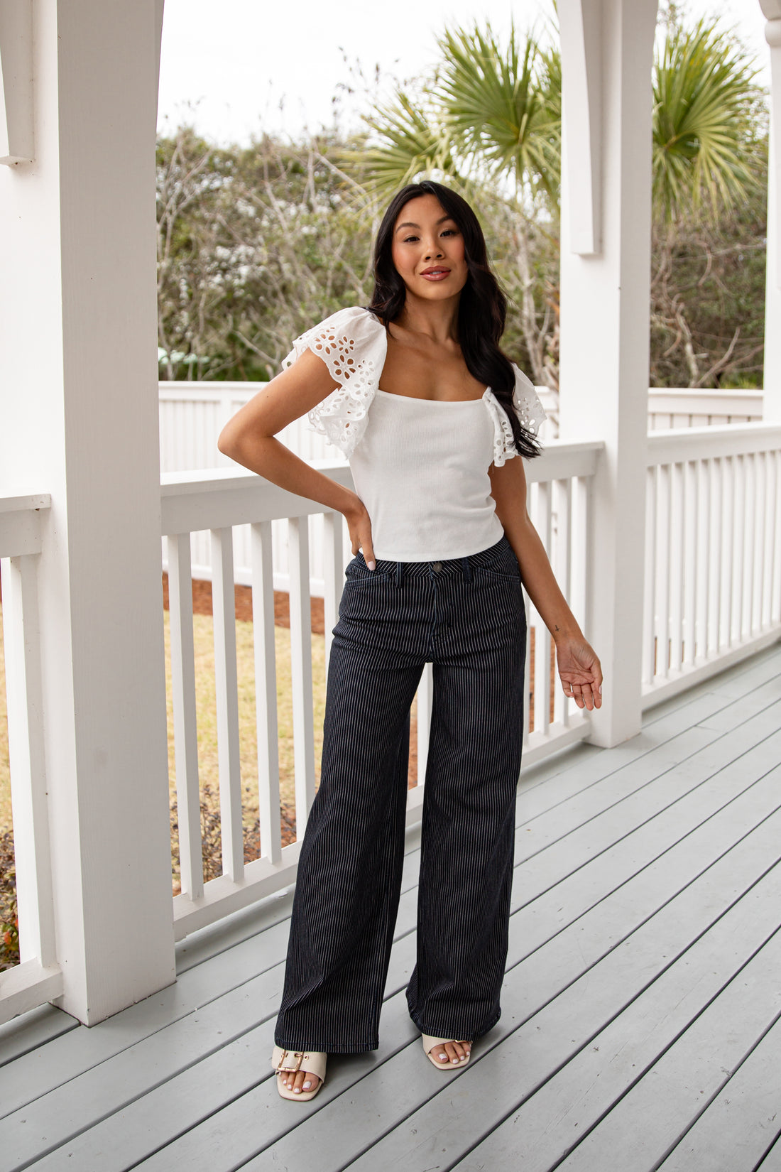 Woman in white top and black pants standing on a porch