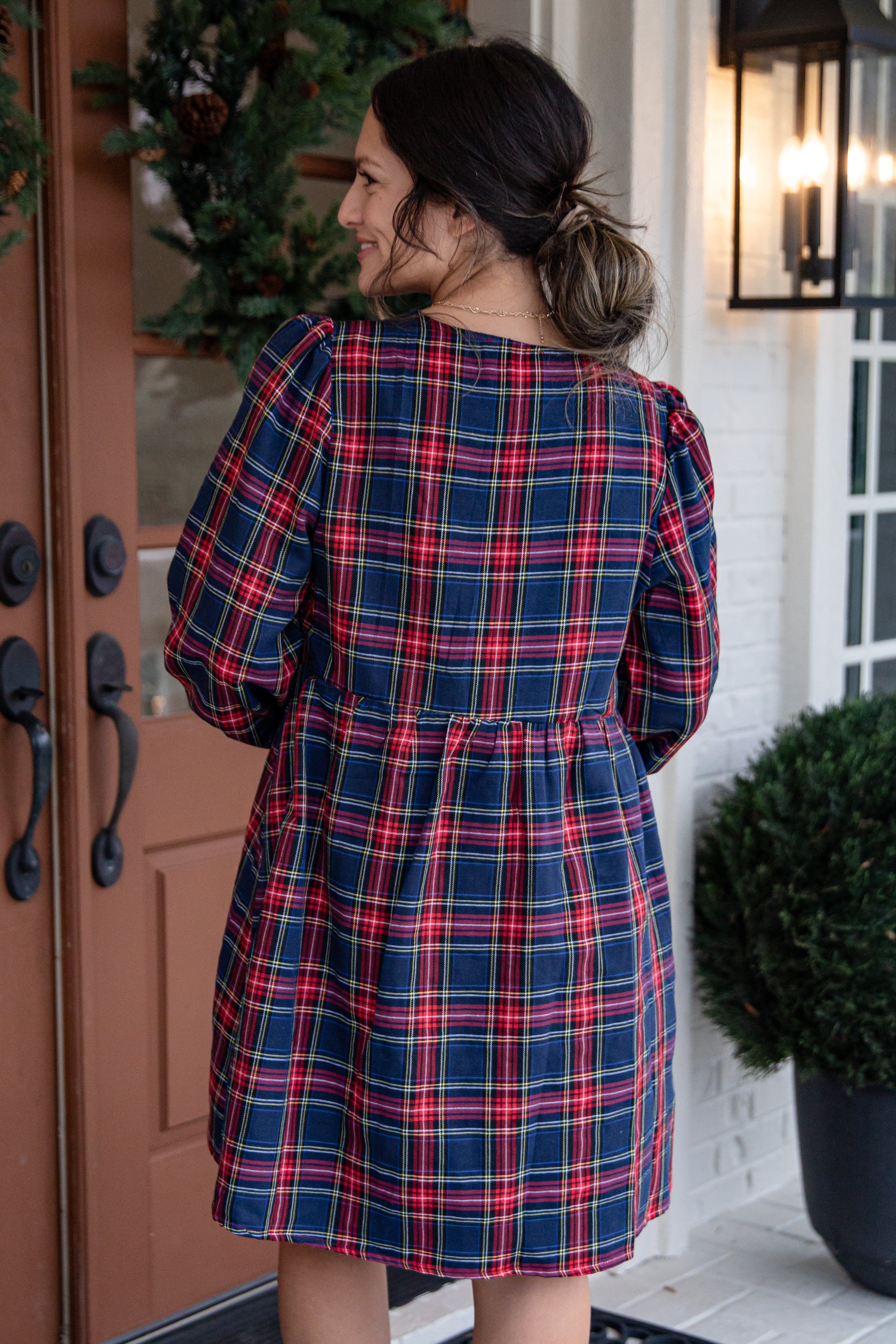Woman wearing a red and blue plaid dress standing in front of a door.