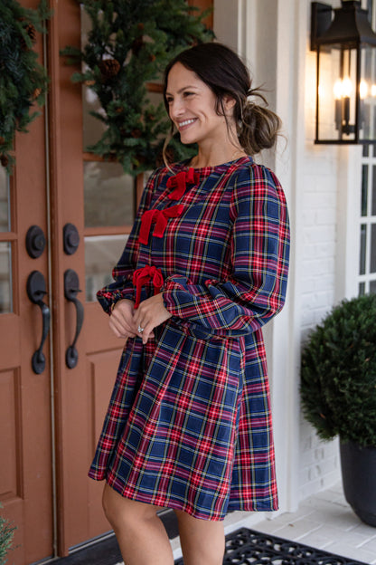 Woman in a plaid dress with red accents standing in front of a door.