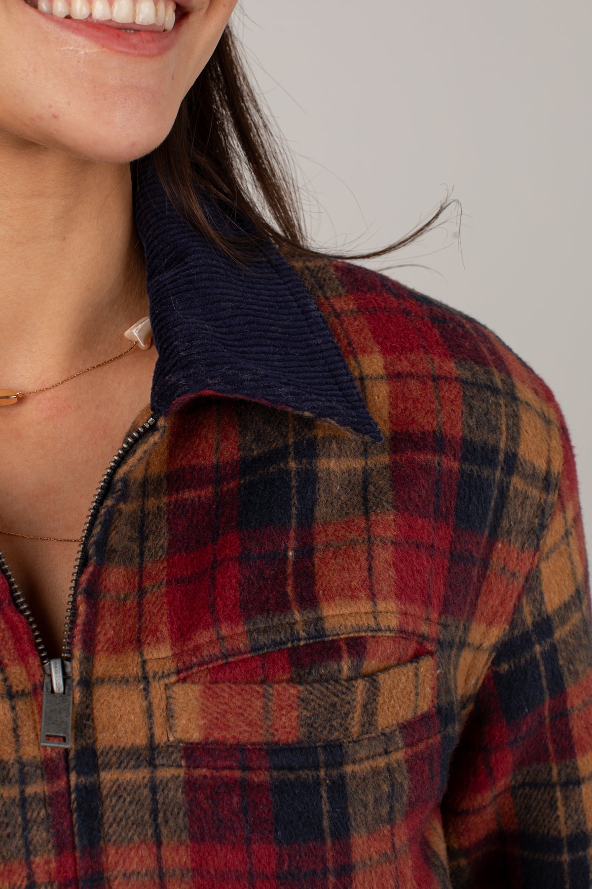 Close-up of a person wearing a plaid zip-front shirt jacket with a dark navy corduroy collar. The plaid pattern features red, brown, and navy tones.