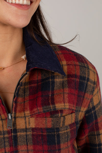 Close-up of a person wearing a plaid zip-front shirt jacket with a dark navy corduroy collar. The plaid pattern features red, brown, and navy tones.