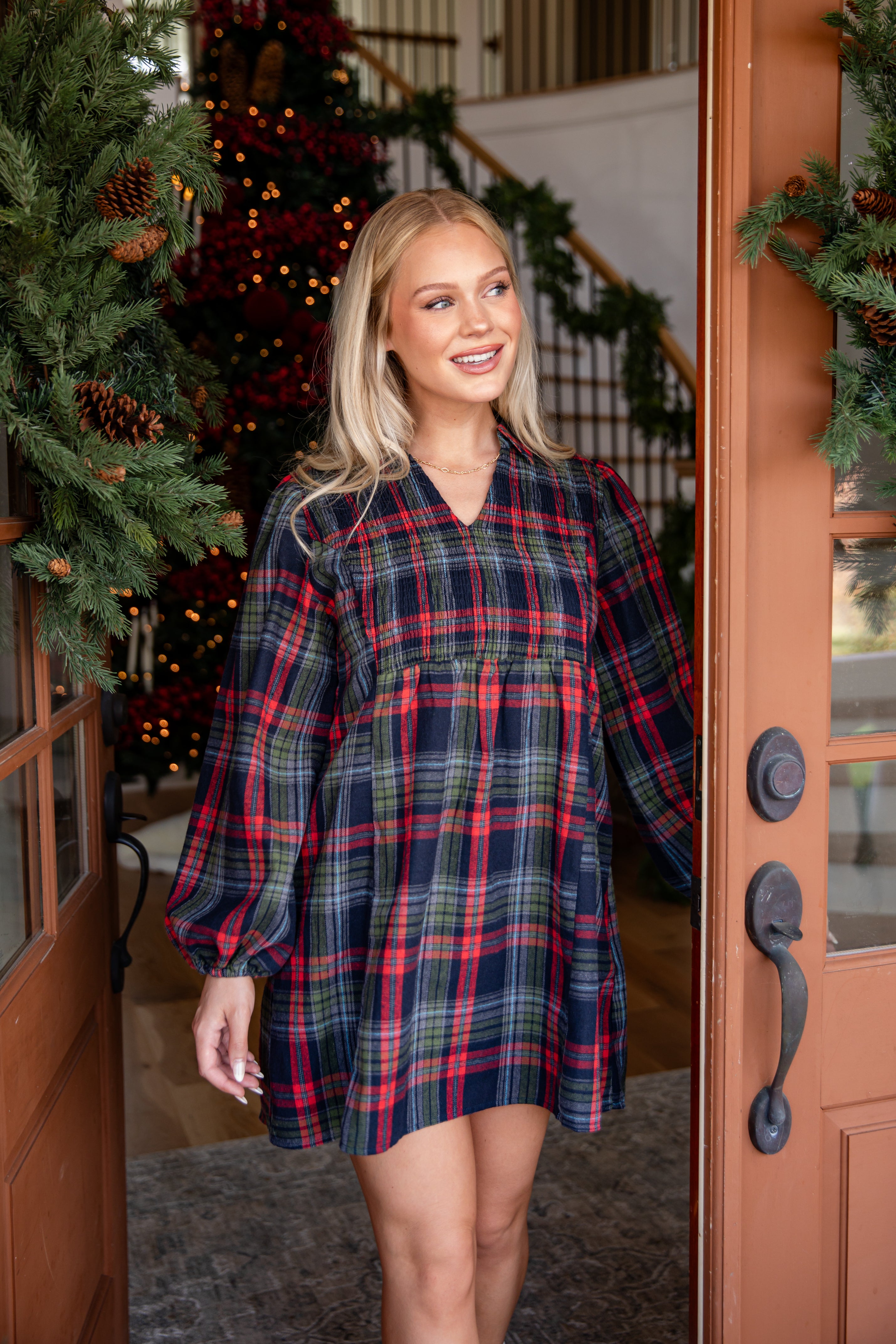 Woman wearing a plaid dress standing in front of a decorated Christmas tree.