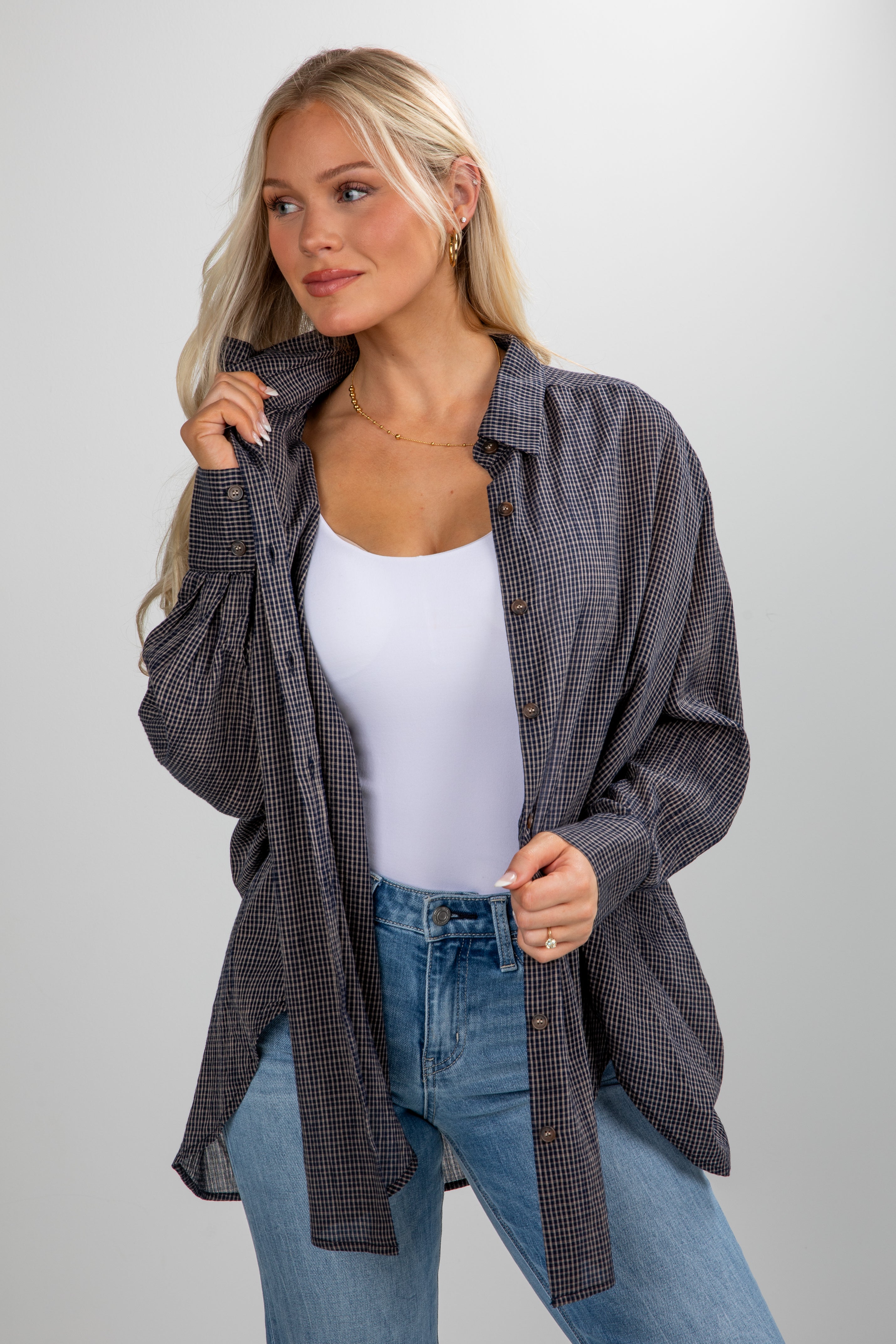 Woman wearing a plaid shirt over a white top and blue jeans on a gray background