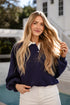 Woman with long blonde hair wearing a navy sweater over a white shirt by a pool.