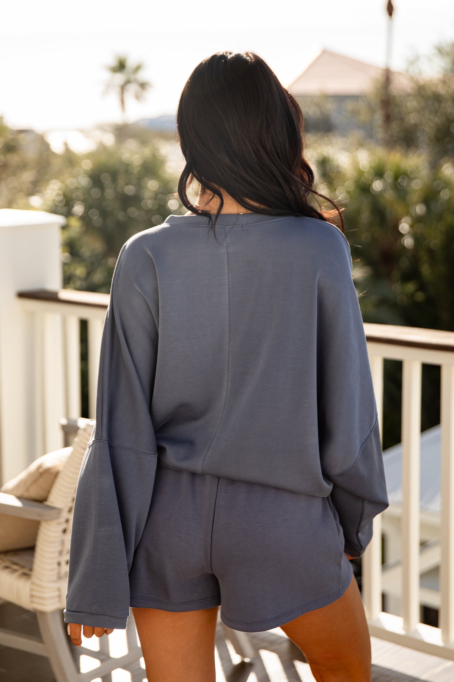 Person wearing a gray outfit on a balcony with greenery in the background