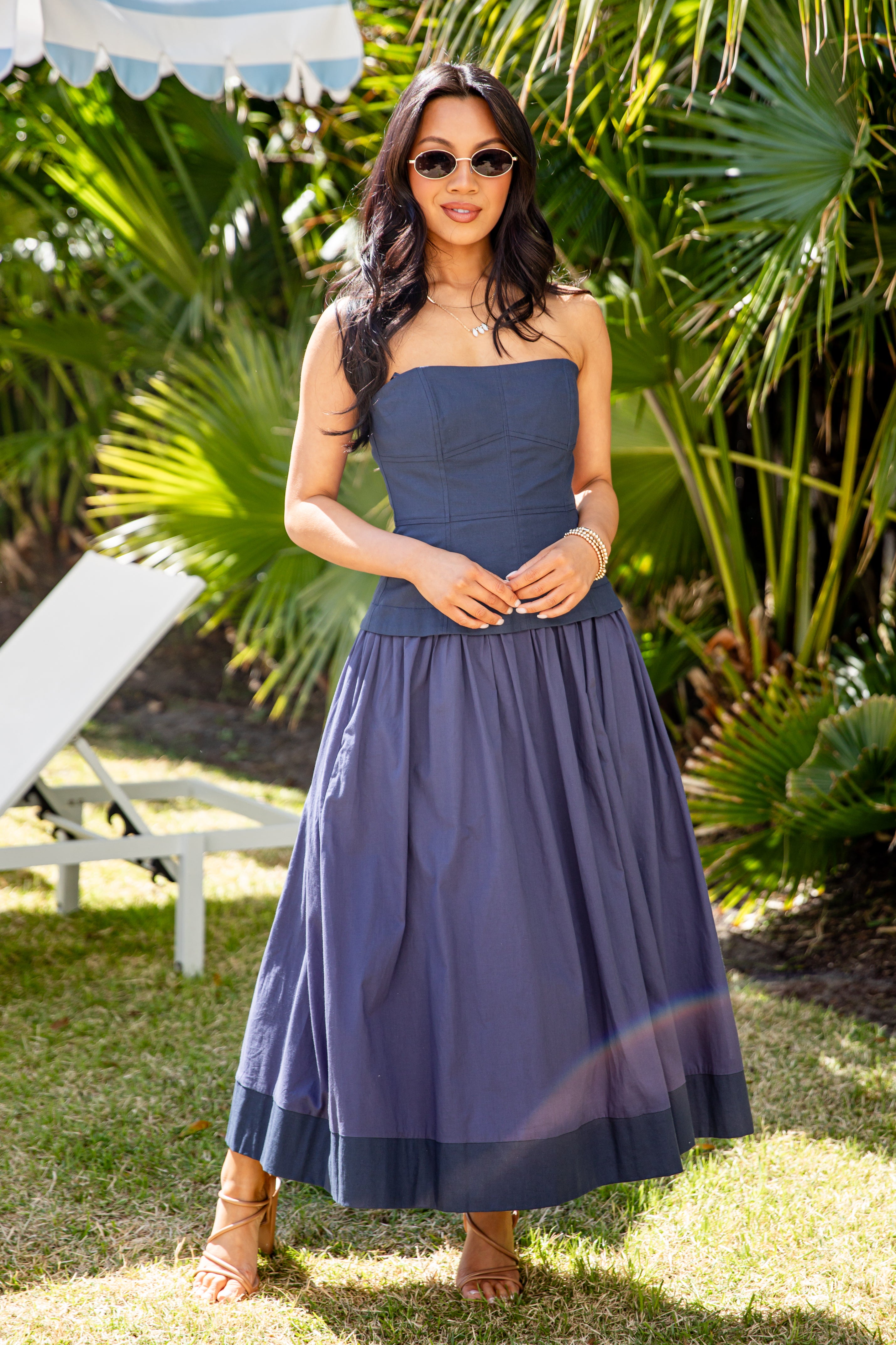 Woman in a blue dress standing outdoors with greenery in the background
