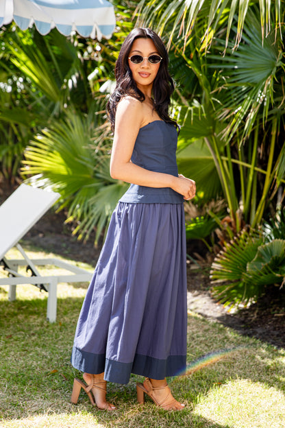 Woman in a blue strapless top and wide-leg pants standing outdoors with greenery in the background