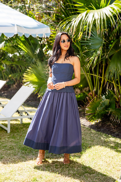 Woman in a blue strapless dress standing in a garden with palm trees and a white umbrella.