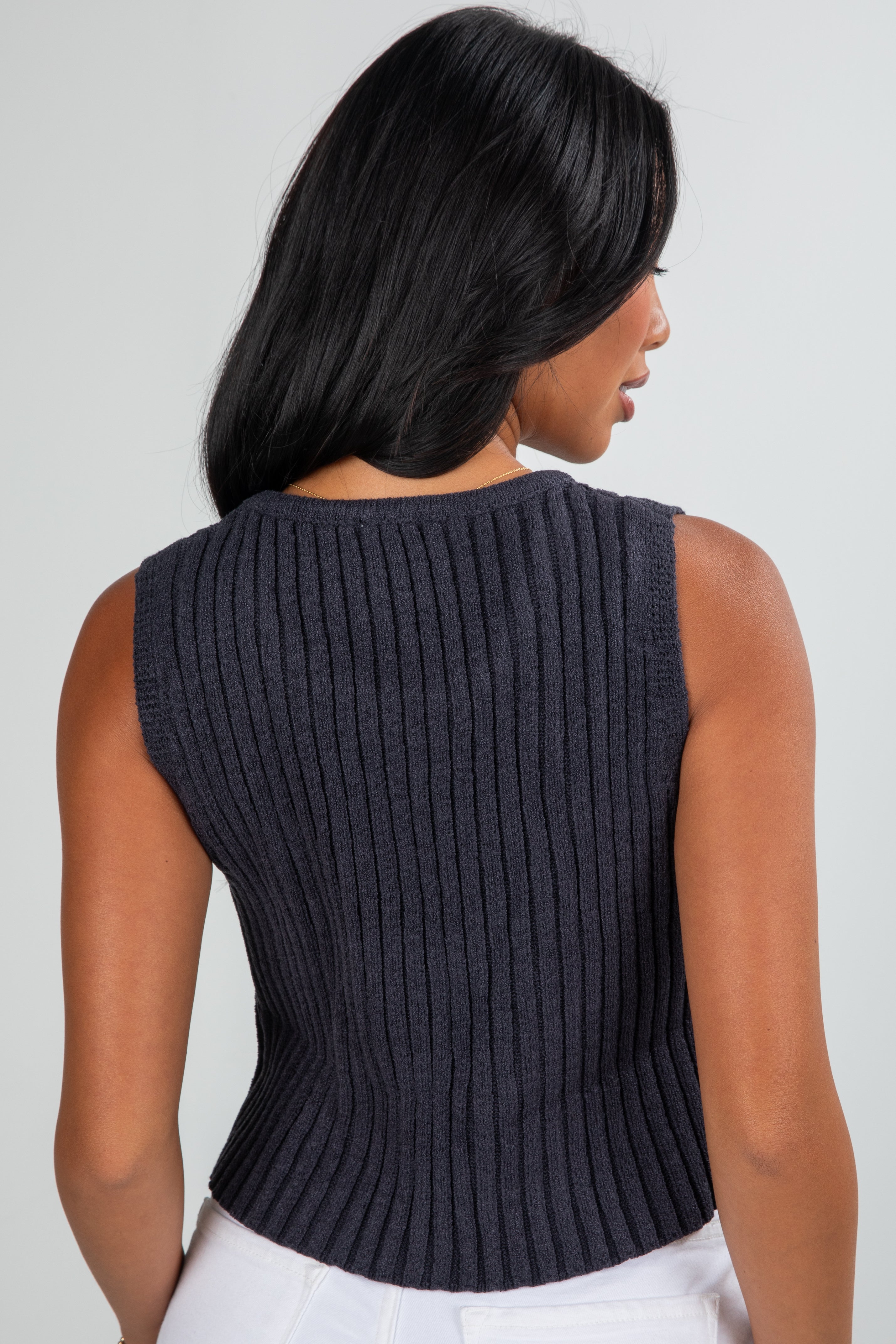 Woman wearing a dark ribbed knit sleeveless top against a plain background