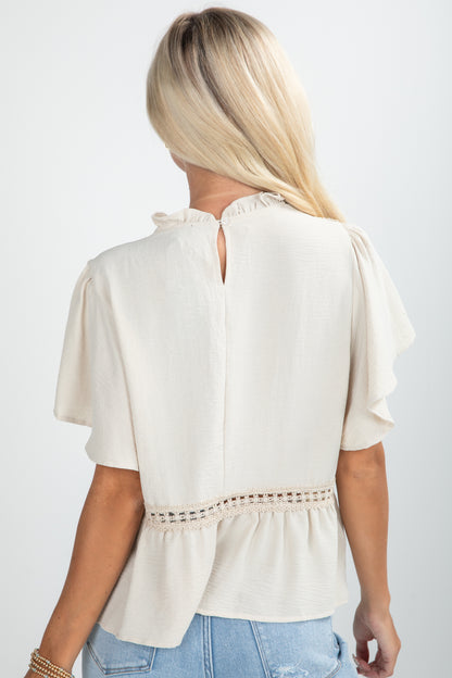 Woman wearing a beige blouse with short sleeves and a subtle pattern on a plain background