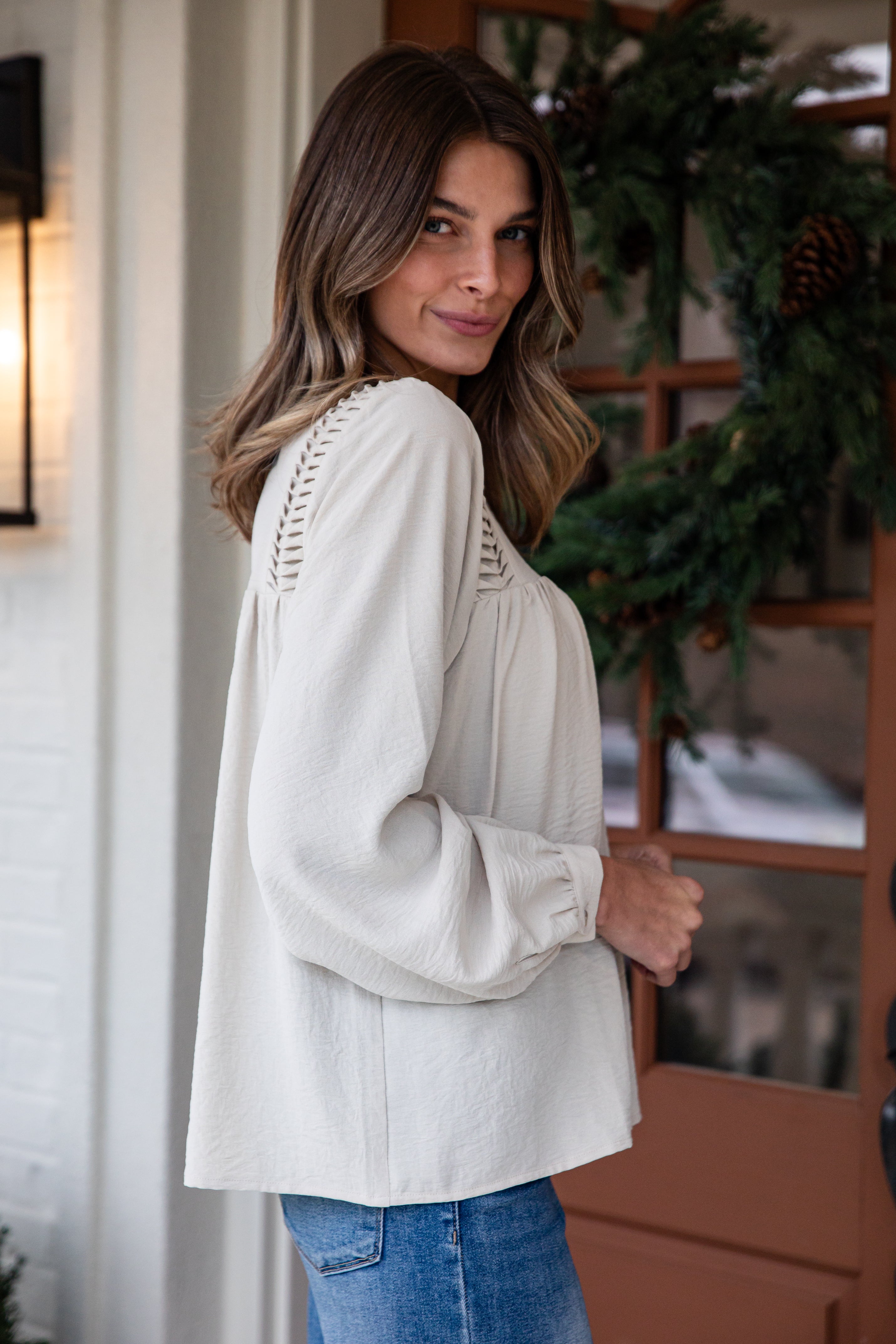 Woman wearing a light-colored blouse with lace details in a home setting.
