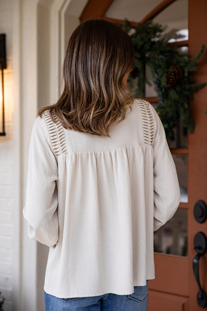 Woman wearing a beige blouse with lace details in front of a door with a wreath.