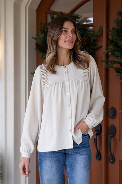 Woman wearing a white blouse and blue jeans standing in front of a wooden door with decorative elements.