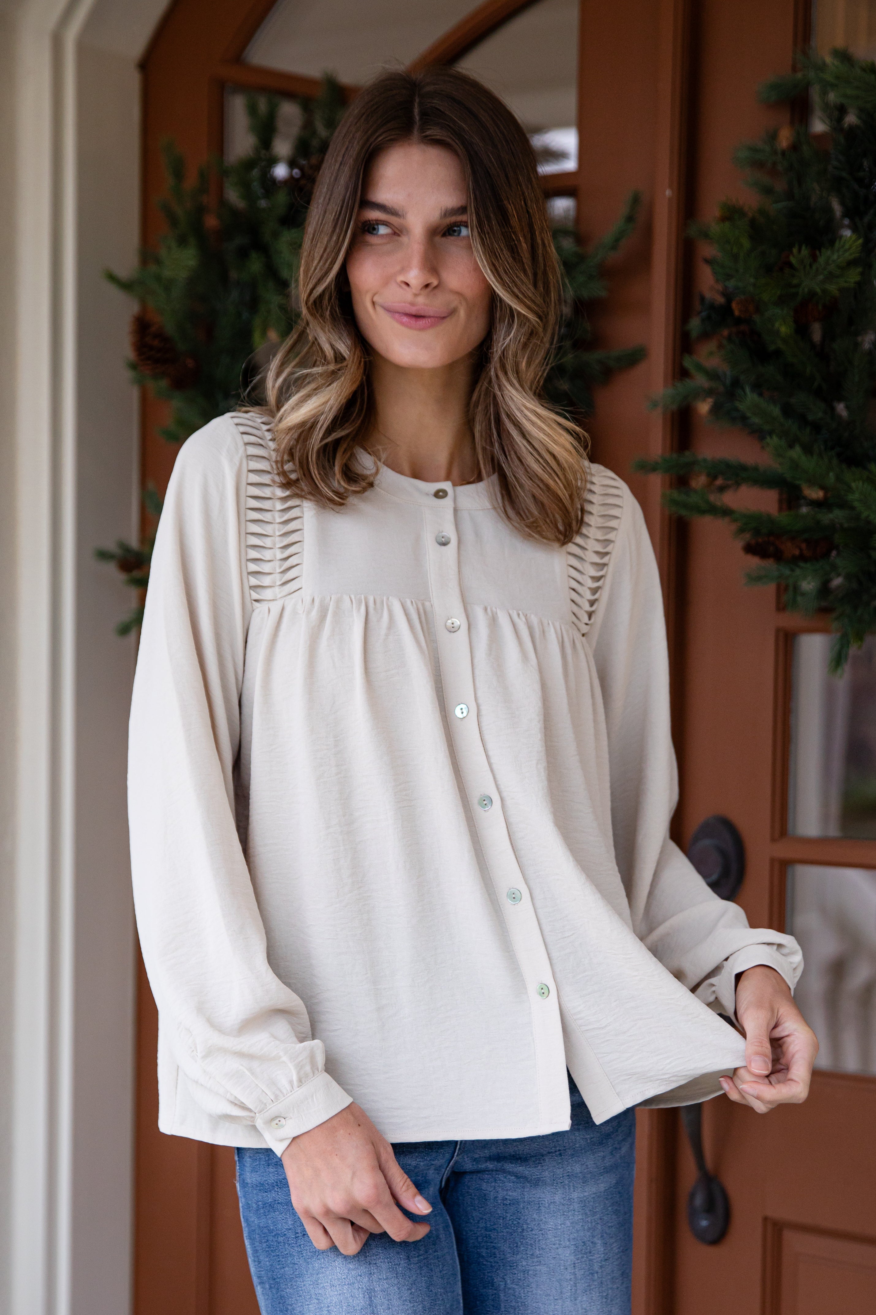 Woman wearing a white blouse with lace details in front of a wooden door.