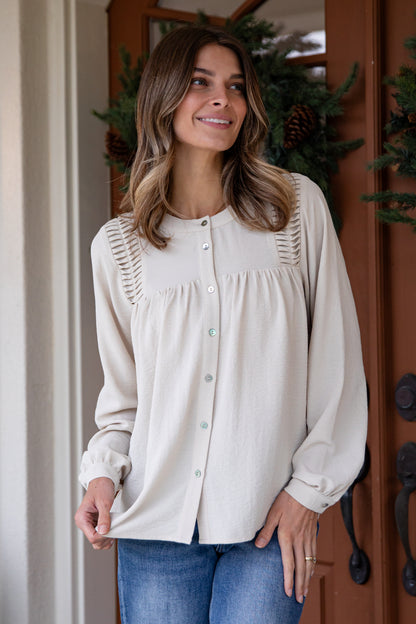 Woman wearing a beige blouse with decorative buttons standing in front of a wooden door.