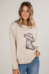 Woman wearing a beige sweater with a cowboy boot design on a plain background