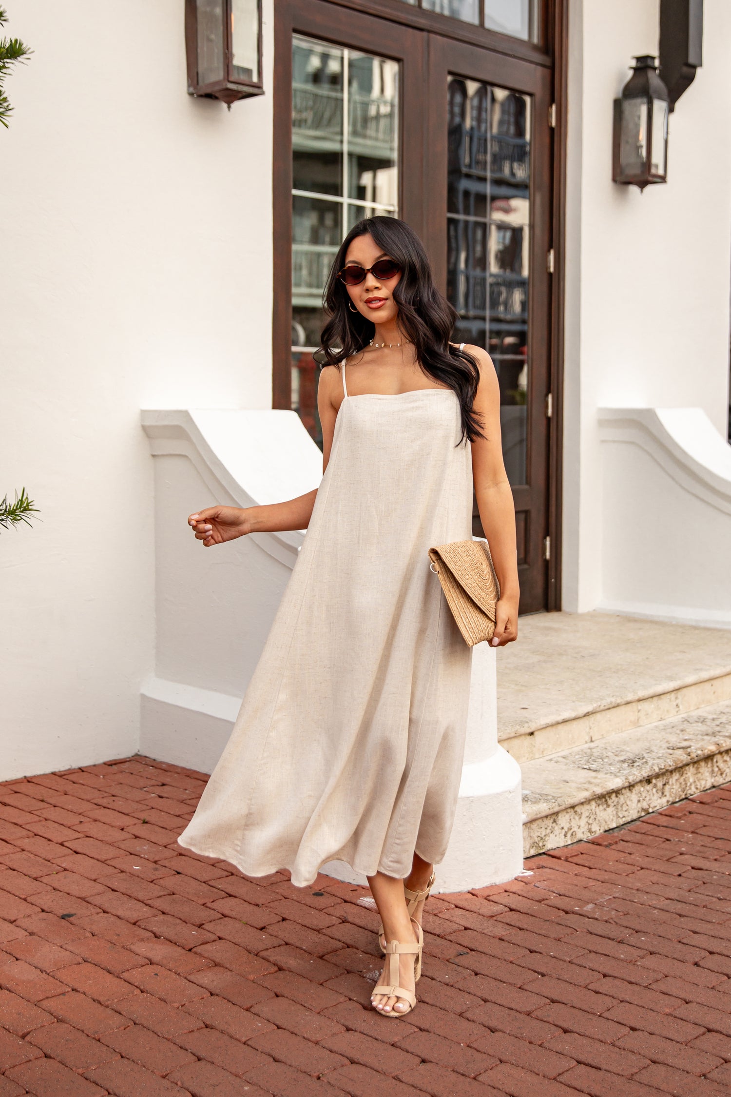 Woman in a beige dress walking on a brick path outside a building.