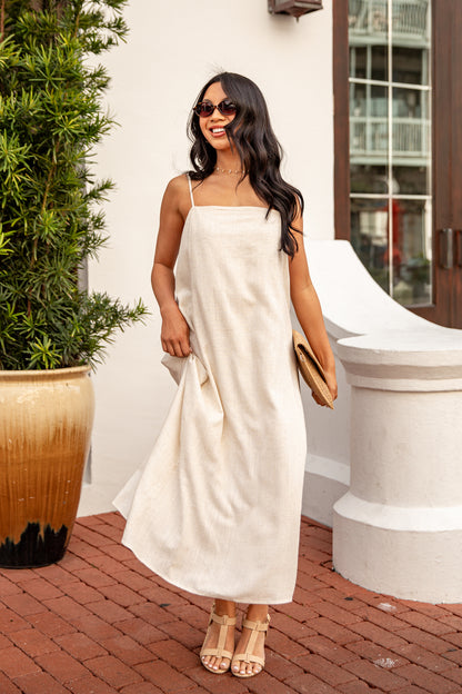Woman in a white dress standing outdoors next to a potted plant.