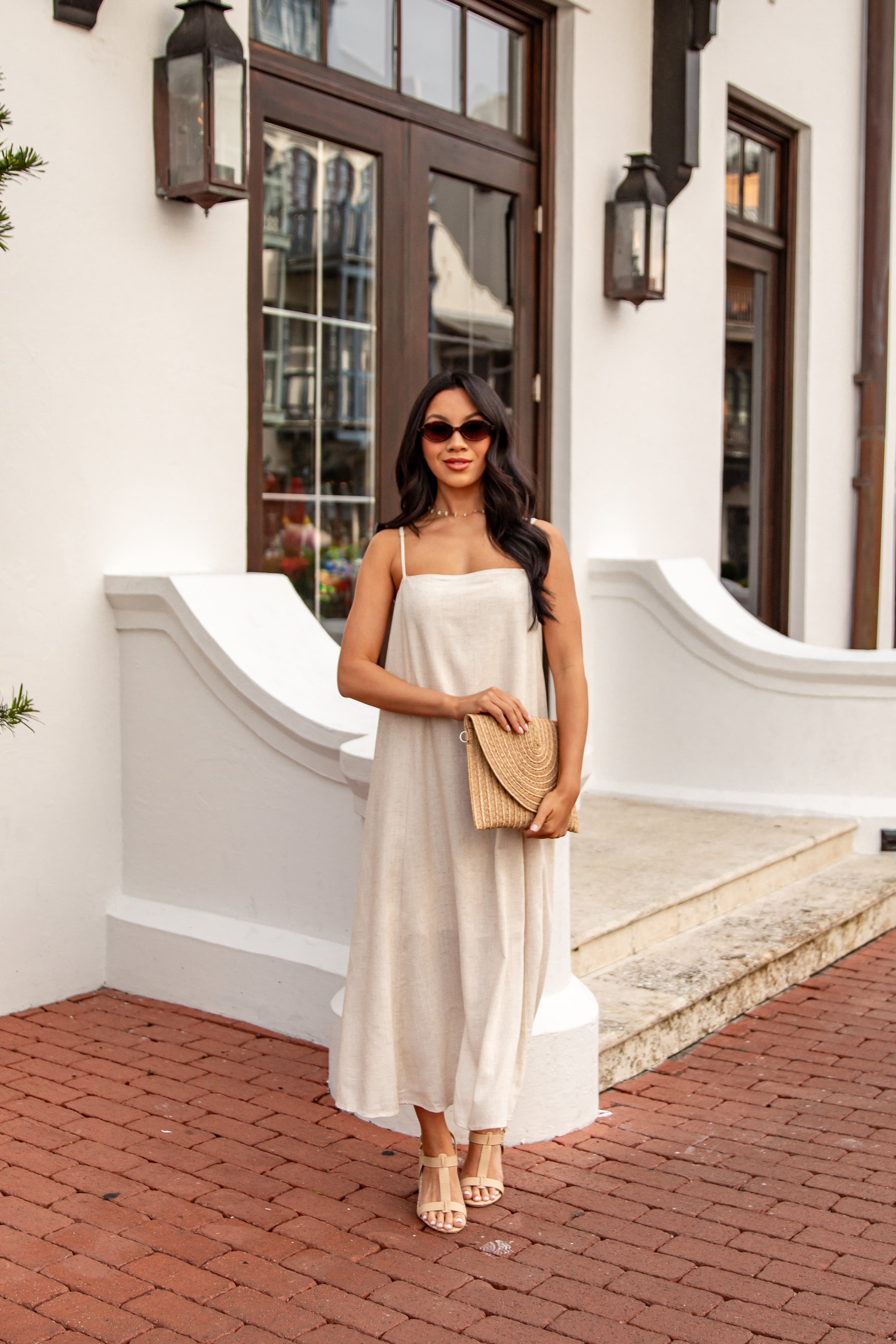 Woman in a white dress holding a beige clutch in front of a building.