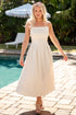 Woman in a white dress standing by a pool with greenery in the background