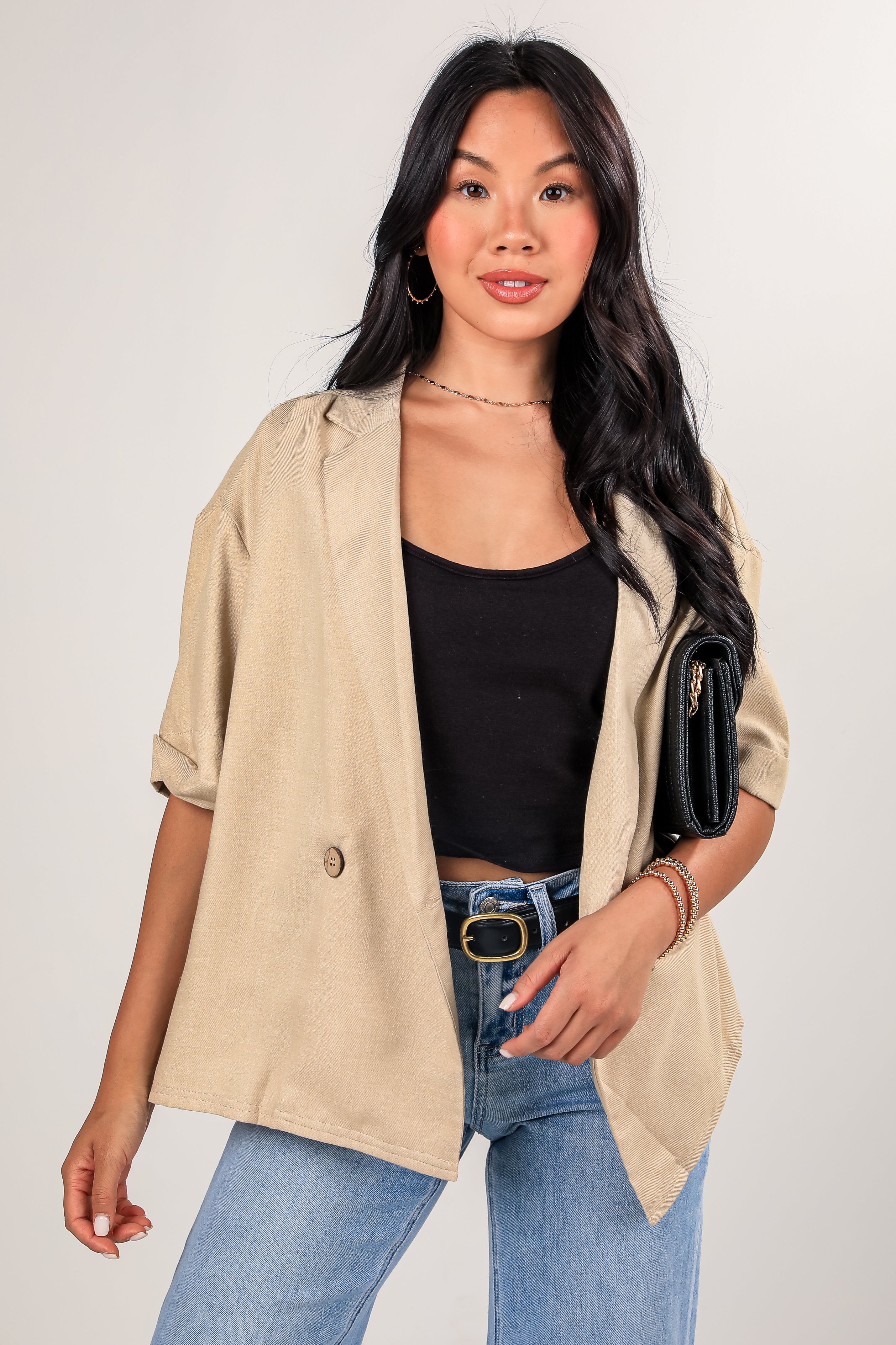 Woman wearing a beige jacket, black top, and blue jeans on a white background