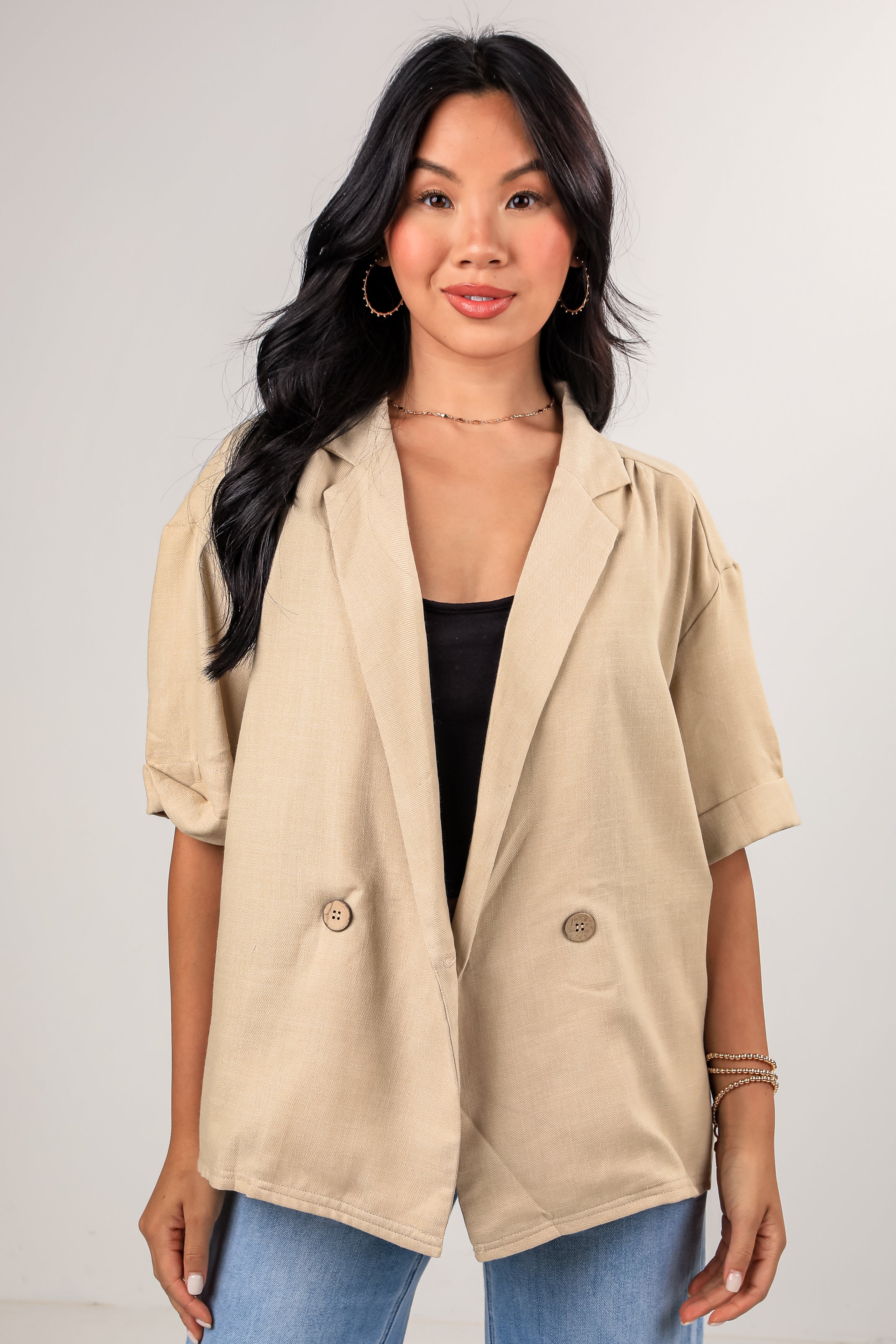 Woman wearing a beige blazer over a black top and blue jeans on a plain background