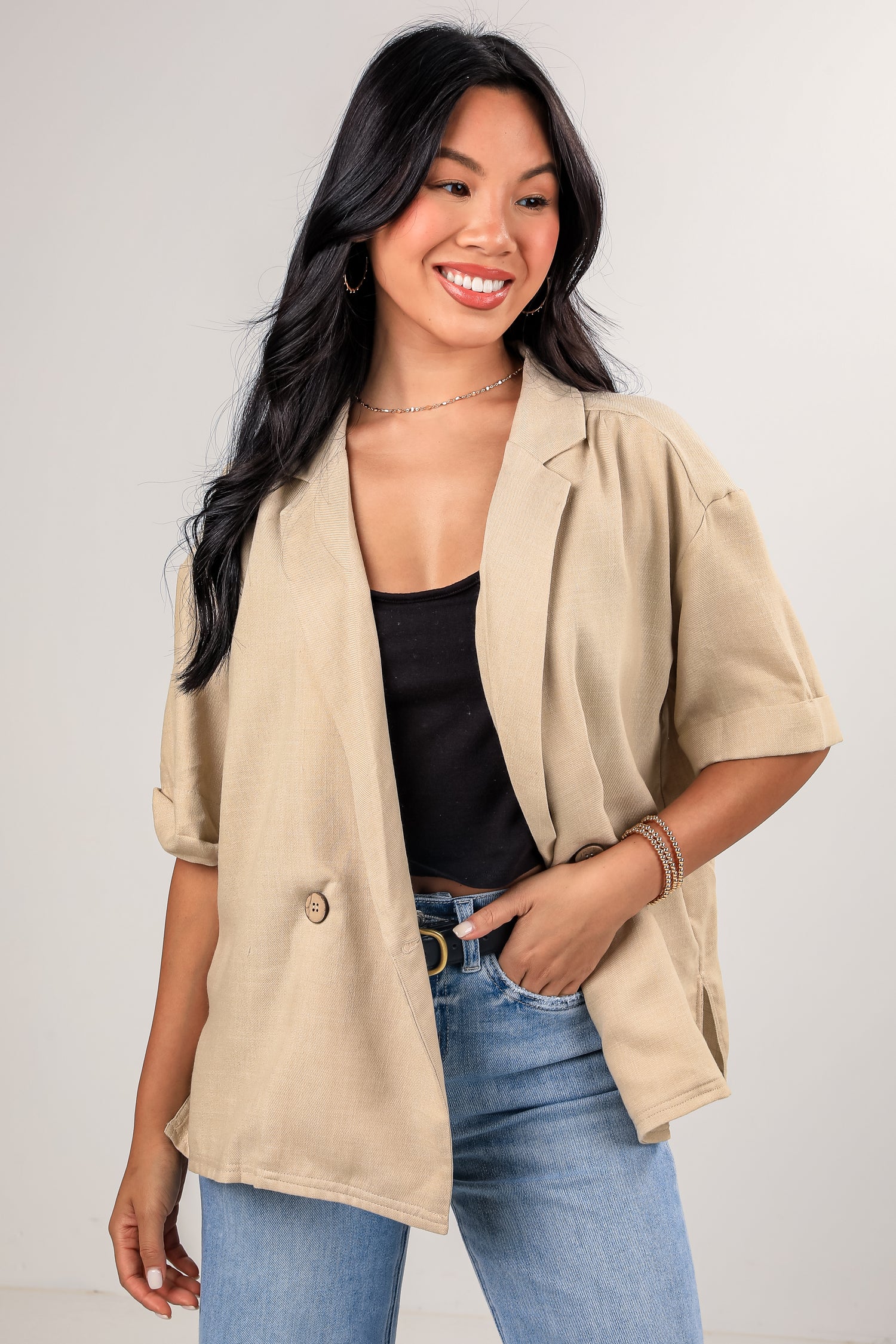Woman wearing a beige blazer over a black top and blue jeans on a plain background